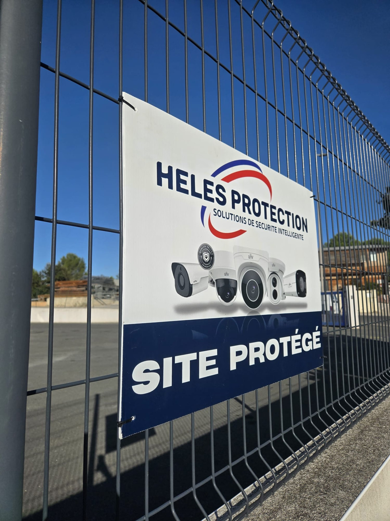 Panneau Site protégé HELES PROTECTION posé sur la clôture du garage poids lourds au Crès.